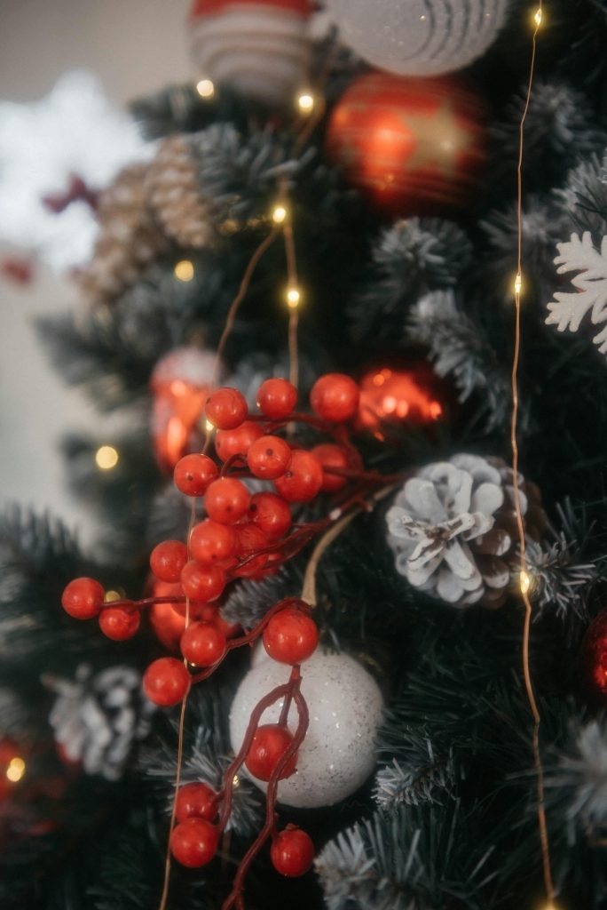 Close-up of Christmas tree with red berries, ornaments, and glowing lights.